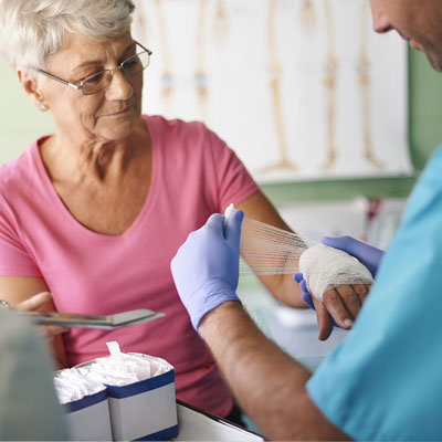 Doctor wrapping elderly womans hand with bandage